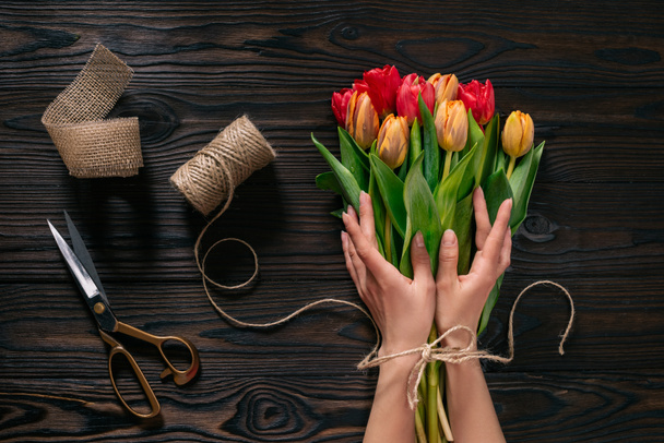 partial view of female hands, rope, scissors and bouquet of flowers on wooden surface - Фото, зображення