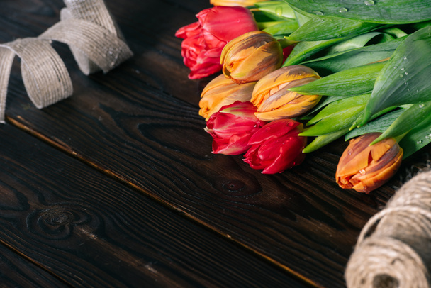 close up view of bouquet of tulips, ribbon and rope on wooden tabletop - Foto, afbeelding