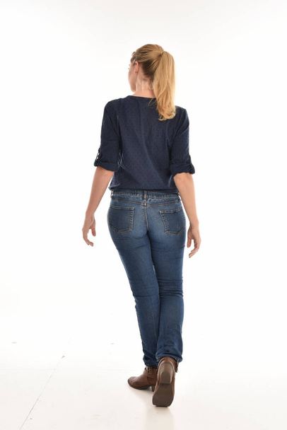 full length portrait of blonde girl wearing simple blue shirt and jeans, standing pose facing away from the camera. isolated on white background. - Foto, Bild