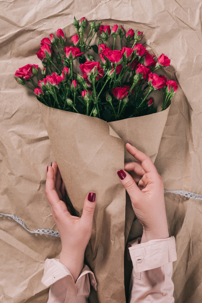 partial view of female hands and bouquet of roses in craft paper - Photo, image