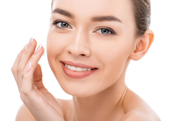 beautiful smiling girl with clean face applying cosmetic cream, isolated on white - Фото, изображение