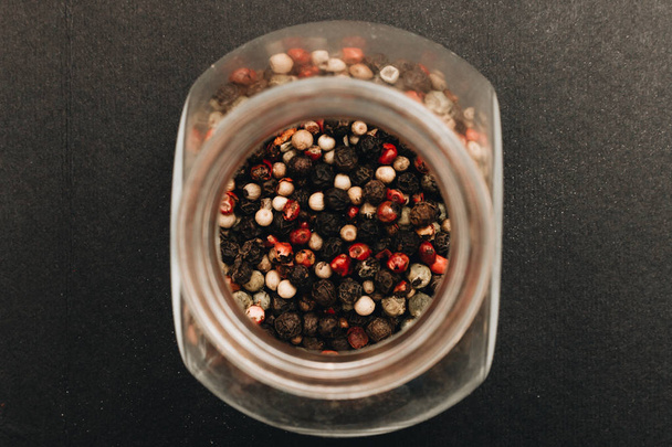 glass can with assorted peppercorns on black background - 写真・画像