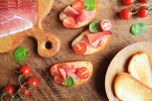 Bruschetta con jamón prosciutto, tomates cherry y espinacas verdes. Vista superior
 - Foto, Imagen