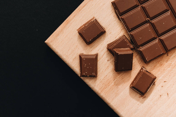 delicious sweet chocolate bar pieces on wooden board - Fotó, kép