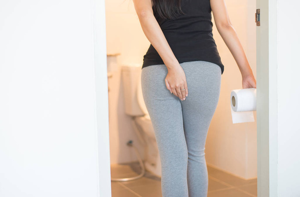 Female holding toilet paper and using toilet in morning,Pants is hanging on her legs - Fotó, kép