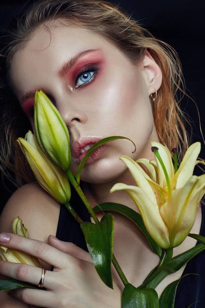 Closeup portrait of woman with flowers lilies in his hands, bright contrasting makeup on the girl's face. Wet hair and clean natural leather. - Valokuva, kuva