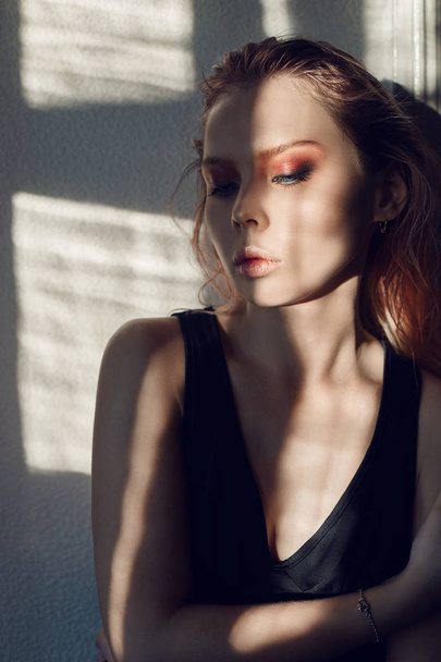 Art fashion contrast portrait of a woman near the window with a shadow on her face. Bright makeup, expressive emotions, mystical, mysterious way. Beautiful big eyes in the sun. - 写真・画像