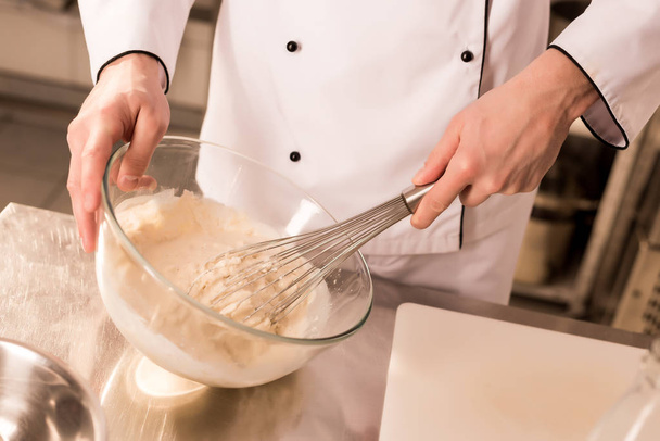 partial view of confectioner with whisk making dough in restaurant kitchen - Foto, afbeelding