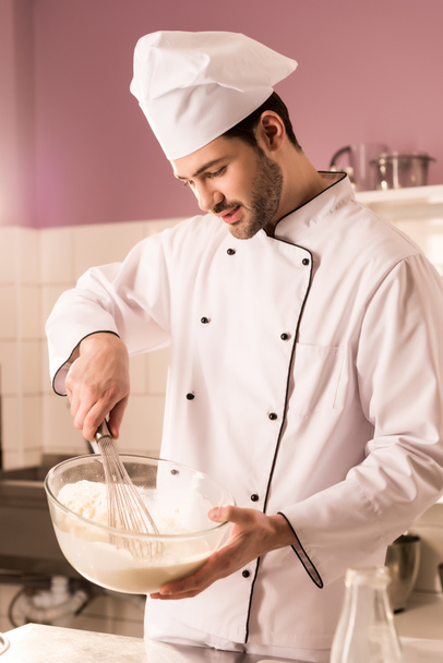 pastelero joven en sombrero de chef haciendo masa en la cocina del restaurante
 - Foto, Imagen