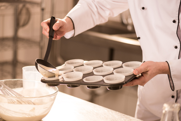 partial view of confectioner pouring dough into baking forms - Foto, Imagem