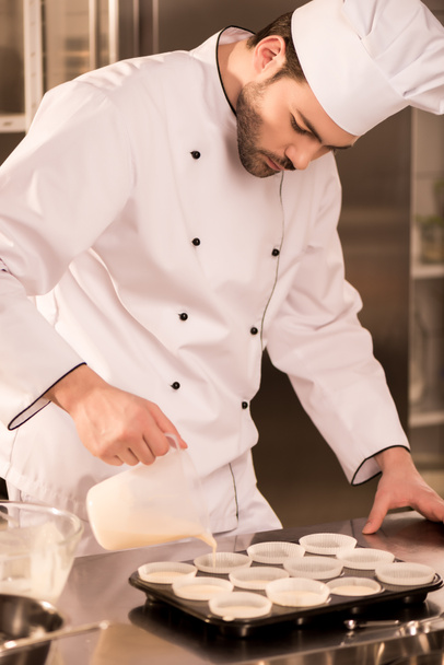 portrait of confectioner pouring dough into baking forms in restaurant kitchen - Photo, Image