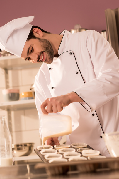 confiseur souriant verser la pâte dans les formes de cuisson dans la cuisine du restaurant
 - Photo, image