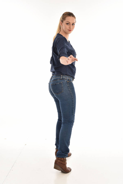 full length portrait of blonde girl wearing simple blue shirt and jeans, standing pose facing away from the camera. isolated on white background. - Foto, afbeelding