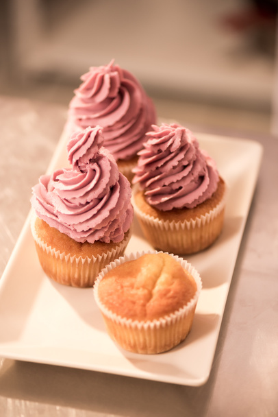 close up view of sweet cupcakes on plate on counter in restaurant kitchen - Foto, afbeelding