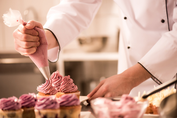 cropped shot of confectioner putting cream on cupcakes - Foto, afbeelding