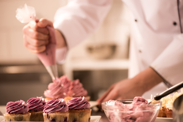 cropped shot of confectioner putting cream on cupcakes - Foto, afbeelding