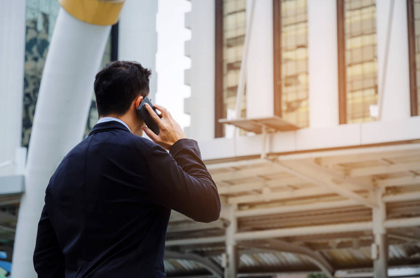 back view of young smart business man wearing black suit making phone call with mobile smart phone in building city background, internet network connection, technology communication, financial concept - Zdjęcie, obraz