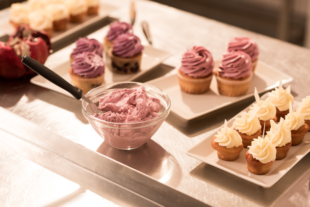 close up view of cream and sweet cupcakes on plates on counter in restaurant kitchen - Fotó, kép
