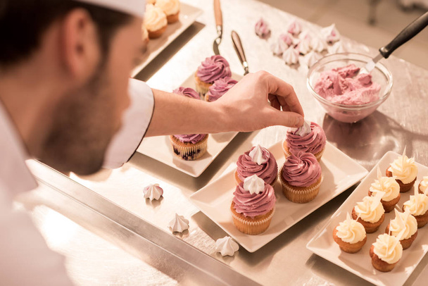selective focus of confectioner decorating cupcakes in restaurant kitchen - Photo, Image