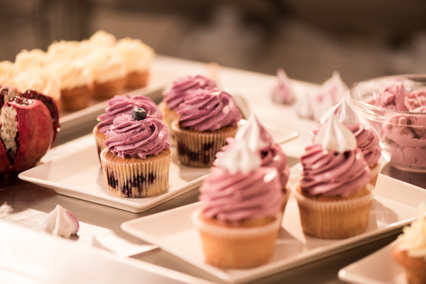 close up view of sweet cupcakes on plates on counter in restaurant kitchen - Fotó, kép