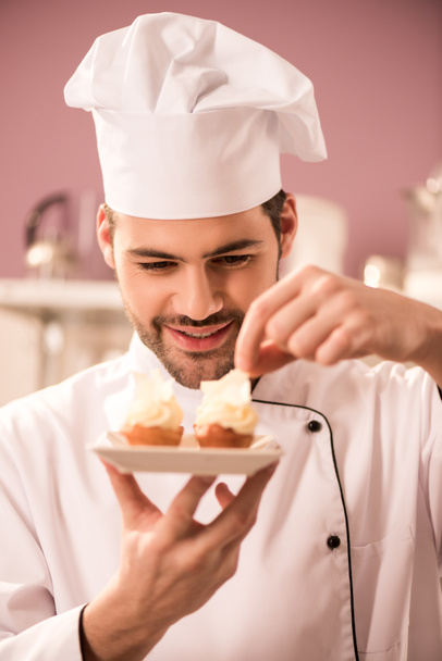 portrait of smiling confectioner decorating cupcakes in restaurant kitchen - Фото, изображение