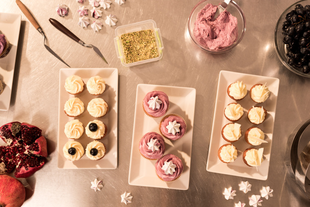 top view of arranged sweet cupcakes on plates on counter in restaurant kitchen - Foto, imagen