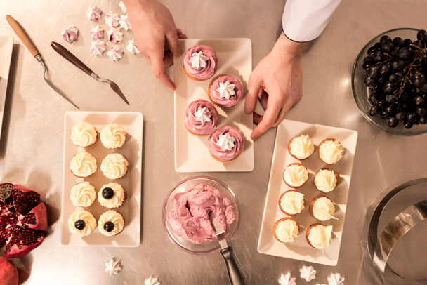 bovenaanzicht banketbakker schikken cupcakes op plaat - Foto, afbeelding