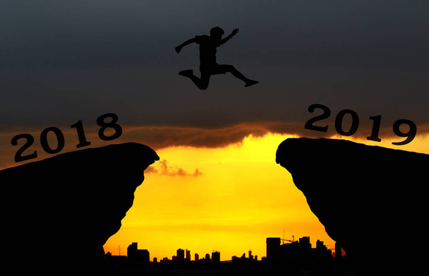 A young man jump between 2018 and 2019 years over the sun and through on the gap of hill silhouette evening colorful sky. happy new year 2018. - 写真・画像