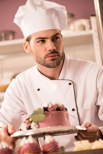 retrato de confitero con pastel en las manos mirando hacia otro lado en la cocina del restaurante
 - Foto, Imagen