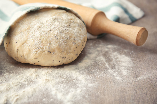 Raw dough with poppy seeds and rolling pin on table - Фото, изображение