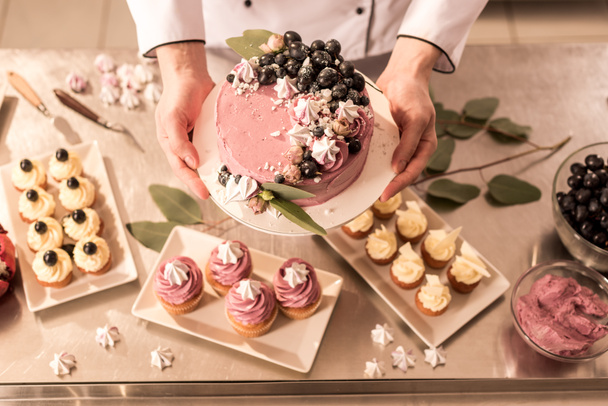 partial view of confectioner holding cake in hands in restaurant kitchen - Foto, imagen