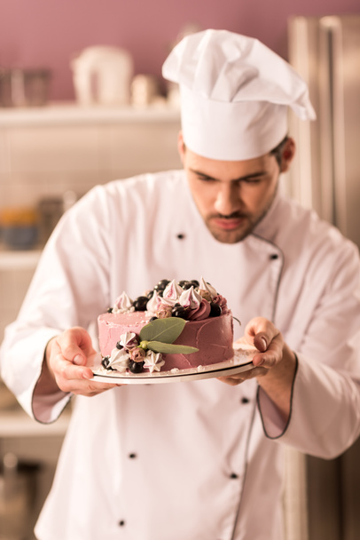 Porträt eines Konditors, der in der Restaurantküche Kuchen in den Händen hält - Foto, Bild