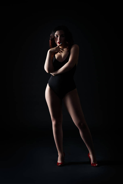 Beautiful sexy woman in bodysuit posing on black background, low key studio shot - Zdjęcie, obraz
