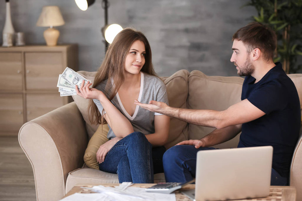 Happy woman with money and indignant man on sofa at home. Problems in relationship - Φωτογραφία, εικόνα