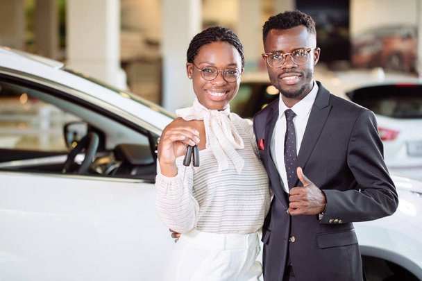 Visiting car dealership. couple holding key of their new car, looking at camera - Фото, зображення