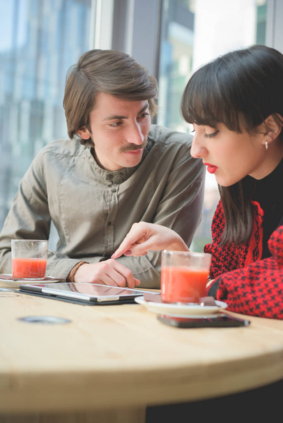 Couple de jeunes beaux caucasiens homme et femme d'affaires collègue assis sur un bar en utilisant tablette et smartphone
  - Photo, image