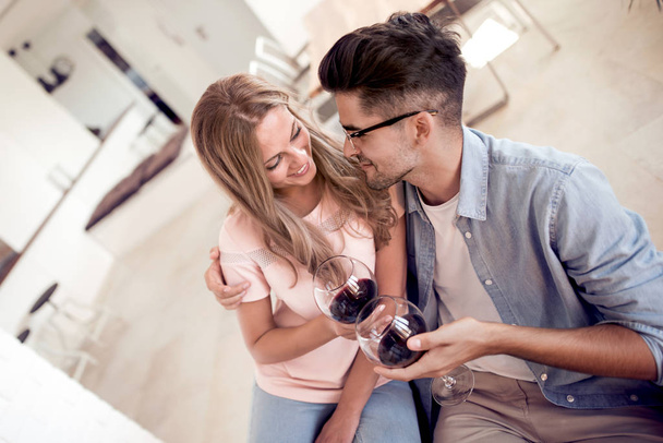 Beautiful young couple with glasses of red wine in living room. - Photo, image