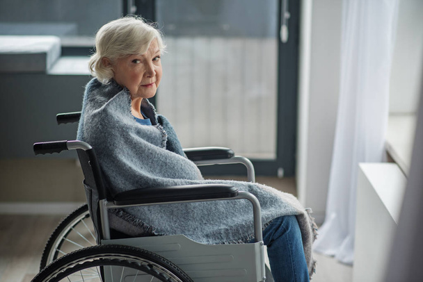Moody old woman sitting in wheelchair in room - 写真・画像