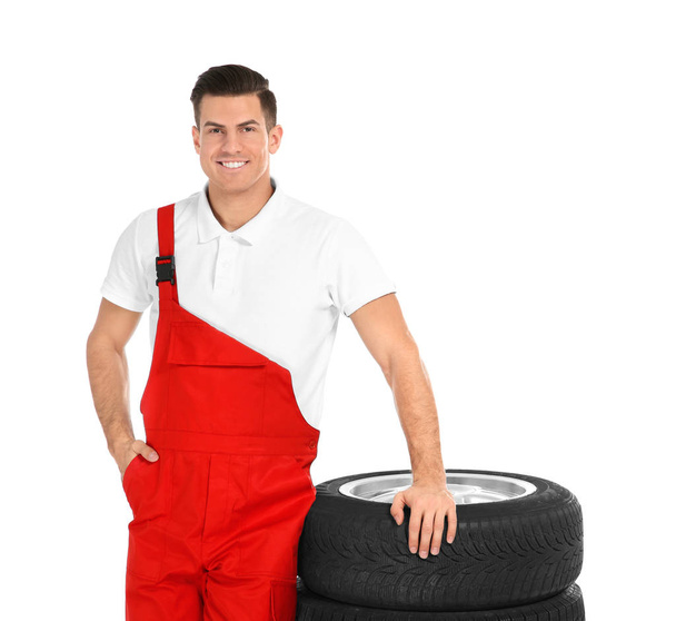 Young mechanic in uniform with car tires on white background - Foto, Bild