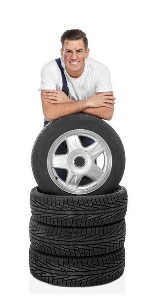 Young mechanic in uniform with car tires on white background - Фото, изображение
