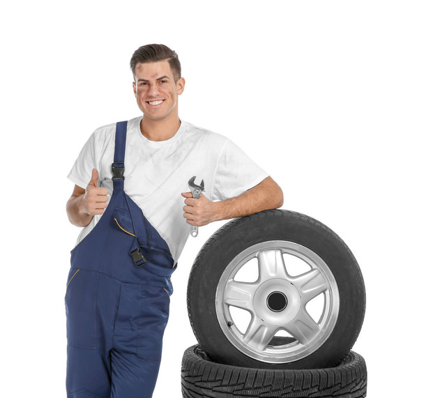 Young mechanic in uniform with car tires on white background - Foto, immagini
