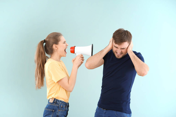 Young woman shouting into megaphone at man on color background. Problems in relationship - Fotó, kép