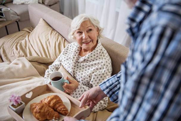 Calm senior man bringing breakfast to woman in bed - Foto, Bild