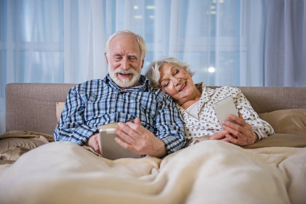 Tranquil elderly couple surfing the internet in bedroom - Fotó, kép