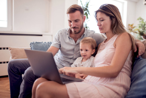 Portret radosny rodzina za pomocą laptopa, siedząc na kanapie w domu. - Zdjęcie, obraz