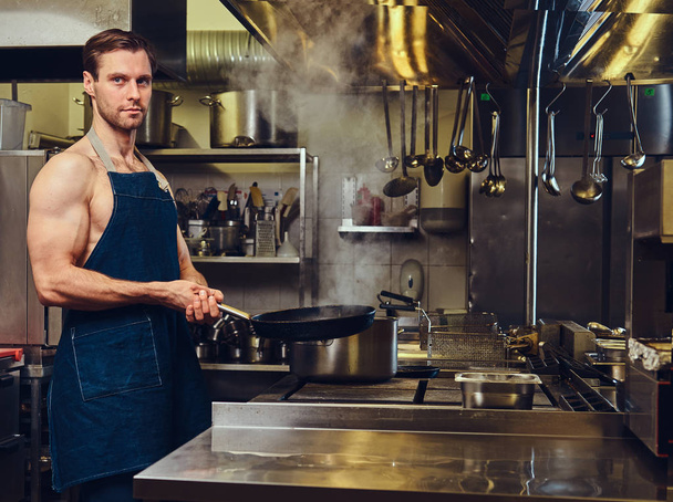 Спортивный шеф-повар держит сухую сковороду на профессиональной кухне отеля
. - Фото, изображение