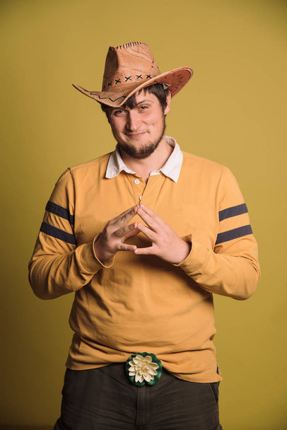 Portrait of big man in a cowboy hat and a yellow shirt. Young man. The studio shot in the yellow wall. - Φωτογραφία, εικόνα