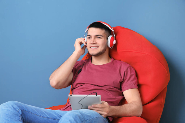 Man listening to audiobook through headphones on color background - Fotó, kép