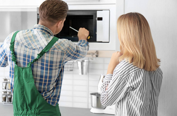Housewife with worker near microwave oven in kitchen - 写真・画像