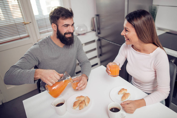 Young happy couple sitting in modern apartment and having breakfast together. - Foto, imagen